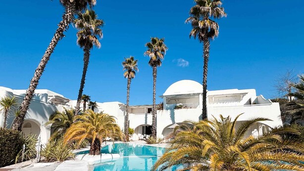 A pool surrounded by palm trees and white buildings with arches. - Holiday apartment with communal pool (Lido di Jesolo)