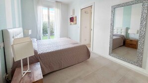 A bedroom with a bed, a nightstand, a mirror, and a window with curtains. - Holiday apartment with communal pool (Lido di Jesolo)