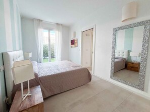 A bedroom with a bed, a nightstand, a mirror, and a window with curtains. - Holiday apartment with communal pool (Lido di Jesolo)