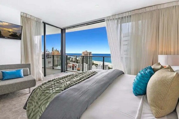 Ein modernes Hotelzimmer mit Balkon, einem Bett mit Kissen, einer Couch und Blick auf die Stadt.