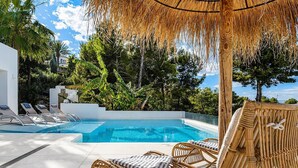 Un área de piscina con sillas de descanso y una estructura cubierta de paja.