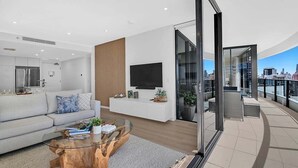 A modern living room with a sofa, coffee table, TV, and a balcony with city views. - Ocean Getaway at Oracle Level 28 (Gold Coast)