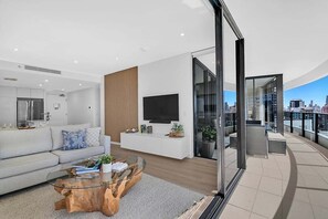 A modern living room with a sofa, coffee table, TV, and a balcony with city views. - Ocean Getaway at Oracle Level 28 (Gold Coast)