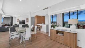 A modern apartment with a dining area, kitchen, living room, and large windows offering a city view. - Beach Breeze Skyhome at Oracle Level 32 (Gold Coast)