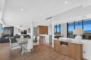 A modern apartment with a dining area, kitchen, living room, and large windows offering a city view. - Beach Breeze Skyhome at Oracle Level 32 (Gold Coast)