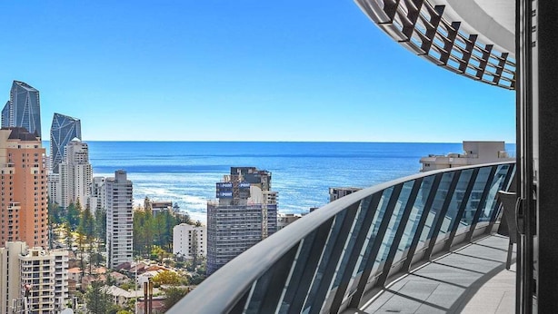 A high-rise building with a glass railing overlooking a cityscape and the ocean. - Beach Breeze Skyhome at Oracle Level 32 (Gold Coast)