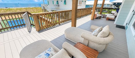 Eine überdachte Terrasse im Freien mit Pool, Liegestühlen und Blick auf den Strand.