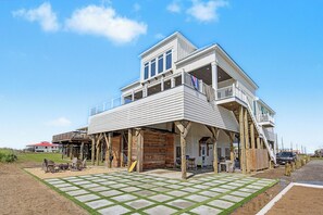 A two-story house with a balcony, a covered patio, and a view of the beach. - Bourbon Bay and Whiskey Lullaby Beachfront, Pool, Pickle Ball Court, Fire Pit and Much More (Grand Isle)