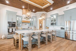 A modern kitchen with a central island, light blue cabinets, stainless steel appliances, and wooden accents. - Bourbon Bay and Whiskey Lullaby Beachfront, Pool, Pickle Ball Court, Fire Pit and Much More (Grand Isle)