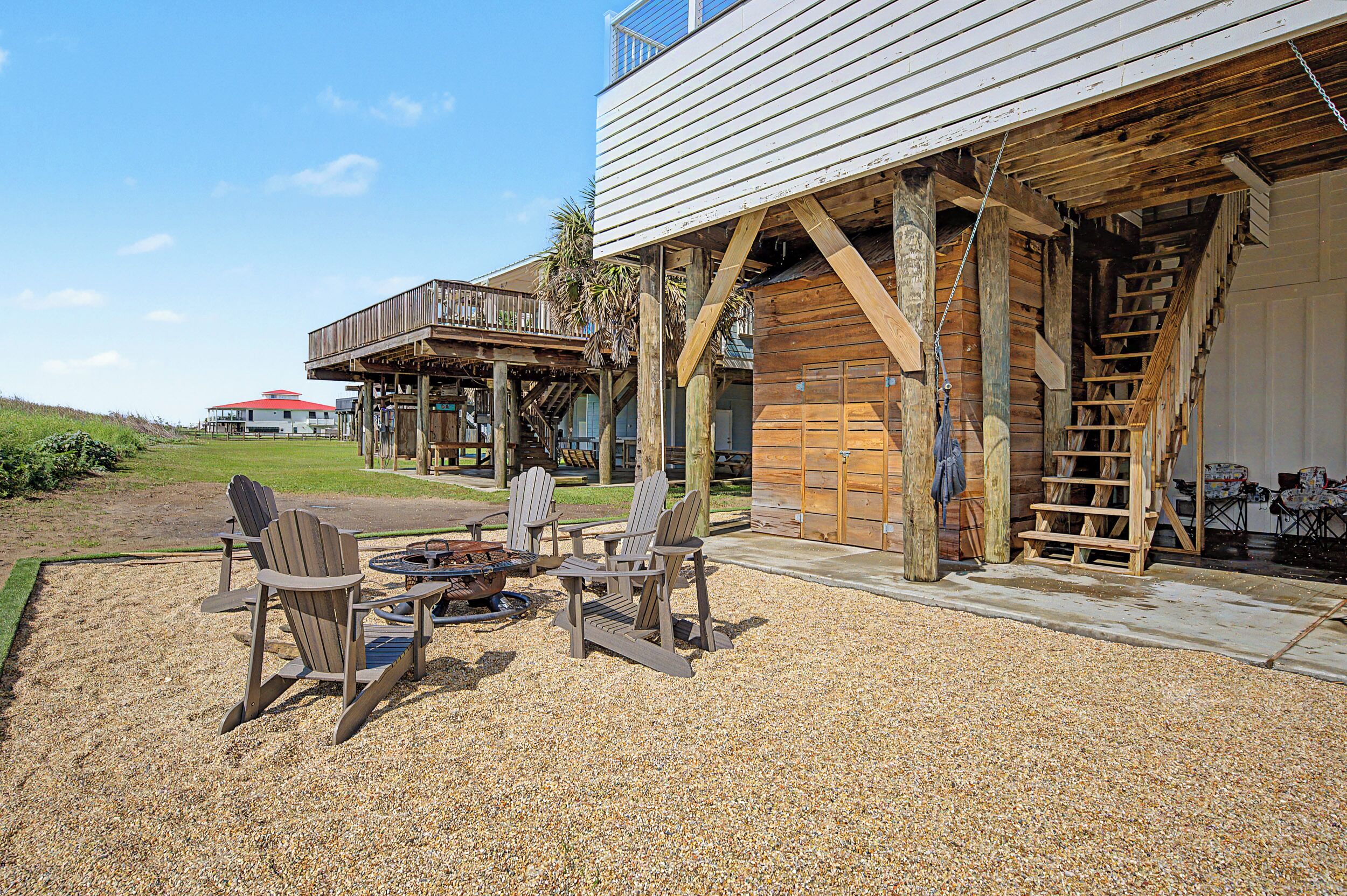 A wooden deck with Adirondack chairs and a fire pit, a covered wooden structure, and a building with a red roof in the background.