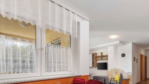 A living room with a large window, a TV mounted on the wall, and a kitchen area in the background. - Holiday flat with balcony and views of greenery (Klimno)