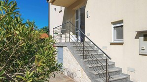 A building with a stone staircase leading to a balcony, a clear blue sky, and some greenery. - Holiday flat with balcony and views of greenery (Klimno)