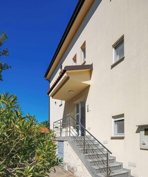 Ein Gebäude mit einer Steinstufen-Treppe, die zu einem Balkon führt, bewölkter, klarer Himmel und etwas Grün.