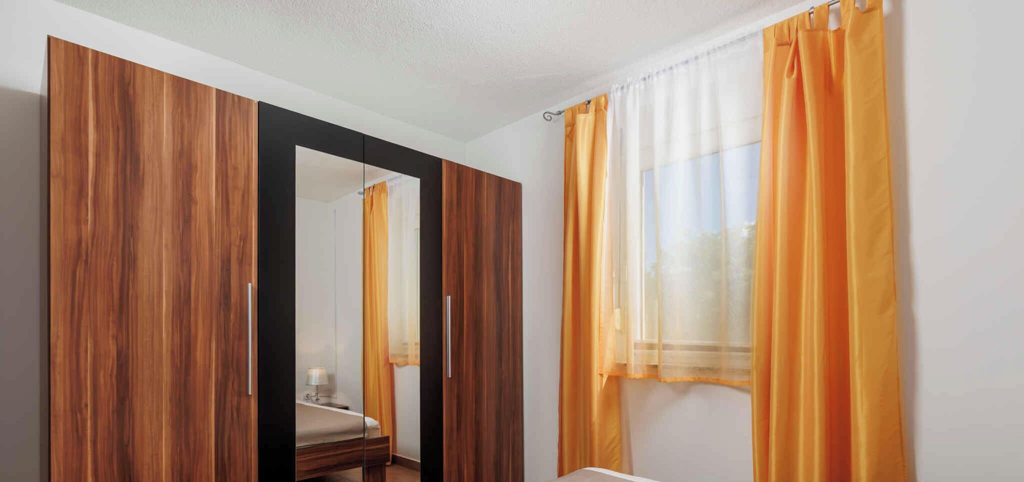A bedroom with a bed, a wardrobe, and a window with curtains.