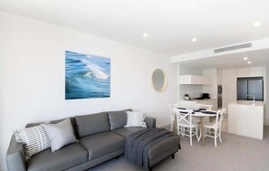 Ein modernes Wohnzimmer mit grauem Sofa, einem Esstisch mit Stühlen, einer Küchenzeile und einem großen abstrakten Gemälde an der Wand.