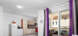 Eine kompakte Küche mit modernen Geräten, ein Essbereich mit Tisch und Stühlen sowie ein Balkon mit violetten Vorhängen.