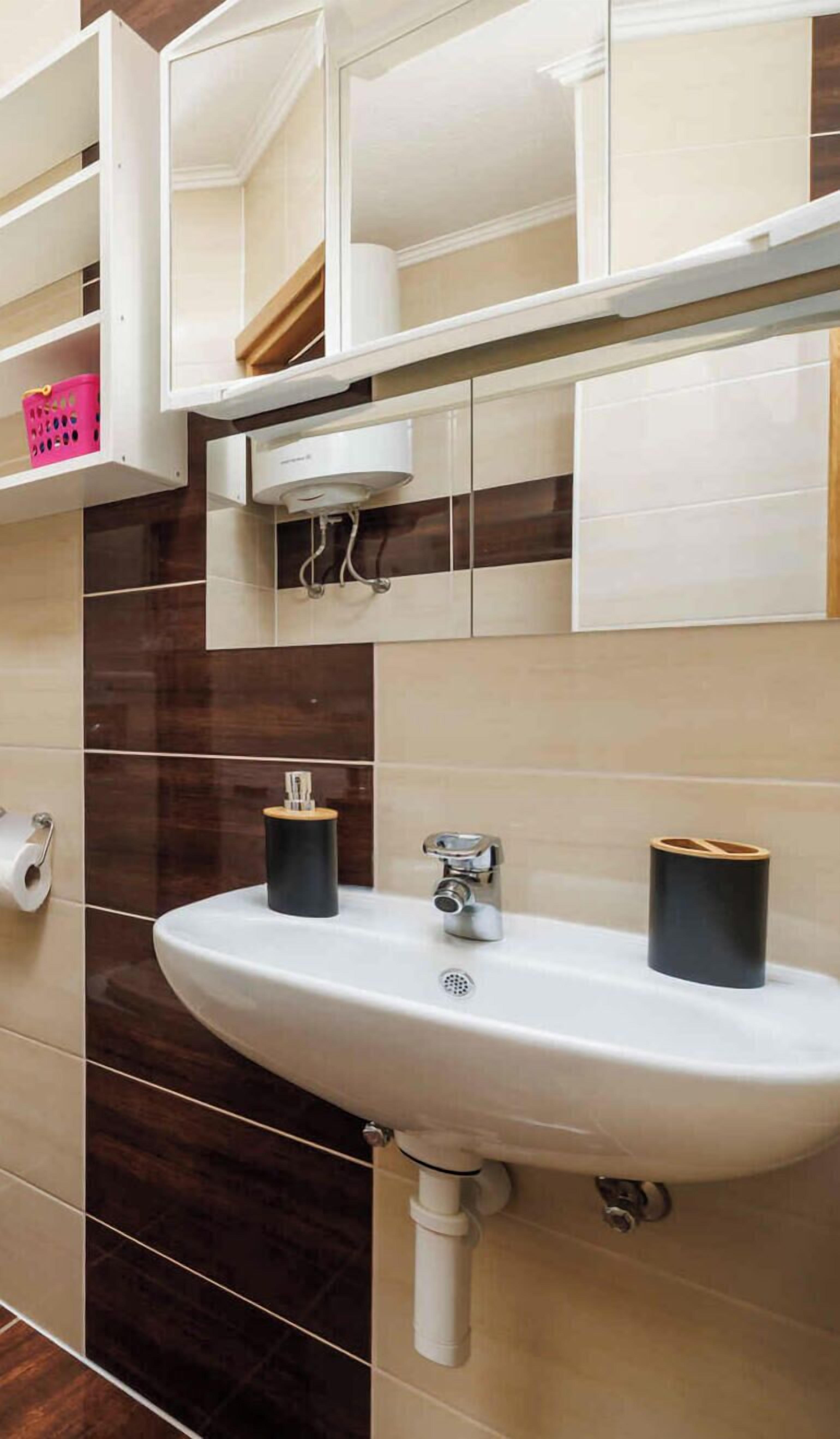 A bathroom with a white sink, two black soap dispensers, a mirror, and a pink basket on a shelf.