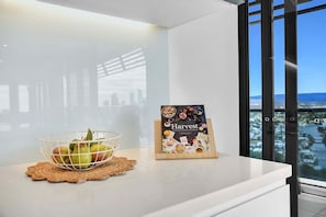 A white countertop with a fruit bowl and a book titled 'Harvest' on a doormat. - Ocean Sunset Skyhome at Oracle Level 33 (Gold Coast)