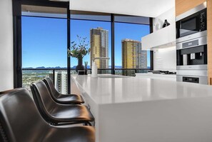A modern kitchen with a view of tall buildings, a white countertop, and a vase with flowers. - Ocean Luxury Skyhome at Oracle Level 36 (Gold Coast)