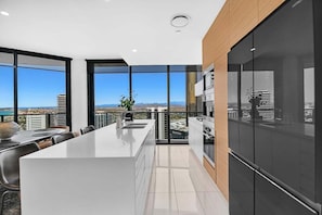 A modern kitchen with a large island, black cabinets, and a view of the cityscape. - Ocean Luxury Skyhome at Oracle Level 36 (Gold Coast)