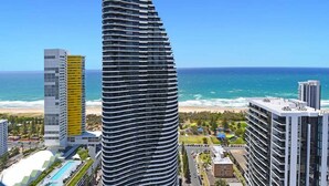Um hotel alto e sinuoso com área de piscina e vista para a praia e oceano.