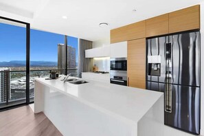 A modern kitchen with a large island, stainless steel appliances, and a view of the cityscape. - Beach Skyhome at Oracle Level 37 (Gold Coast)