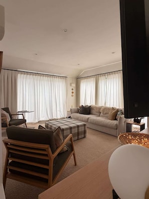 A modern living room with a sofa, ottoman, and a television. - Chartres Holiday (Arrowtown)
