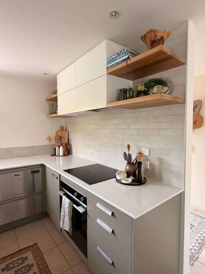 A modern kitchen with white cabinetry, a black countertop, and a backsplash. - Chartres Holiday (Arrowtown)