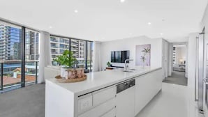 Une cuisine moderne dotée d’un grand îlot central, de meubles blancs et offrant une vue sur les immeubles de grande hauteur.