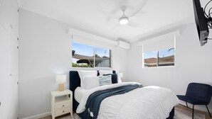 Ein Schlafzimmer mit Bett, Nachttisch, Stuhl und Fenstern.