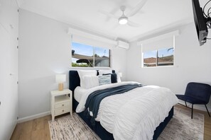 A bedroom with a bed, nightstand, chair, and windows.