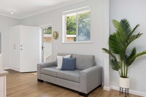 A modern living room with a grey sofa, a potted plant, and a window with a view of greenery.