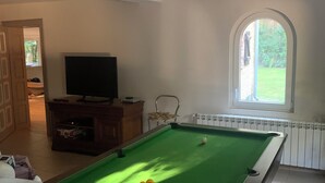 A pool table with balls, a television, and a window with a view of greenery.