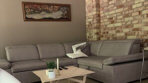 A living room with a grey sofa, a coffee table with a plant, a painting on the wall, and a brick-patterned wall.