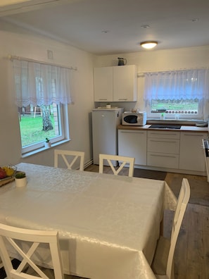 A compact kitchen with white cabinets, a refrigerator, a microwave, and a dining table with chairs. - Forest house in Poland near the lakes. As a couple, with family or friends (Zatom Nowy)