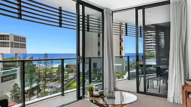 A modern room with a glass door leading to a balcony with a view of the sea and buildings. - Beach Getaway at Oracle Level 6 (Gold Coast)