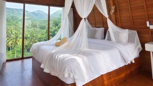 Ein Schlafzimmer mit Holzbalkendecke, einem Baldachinbett und Blick auf eine üppige Landschaft.