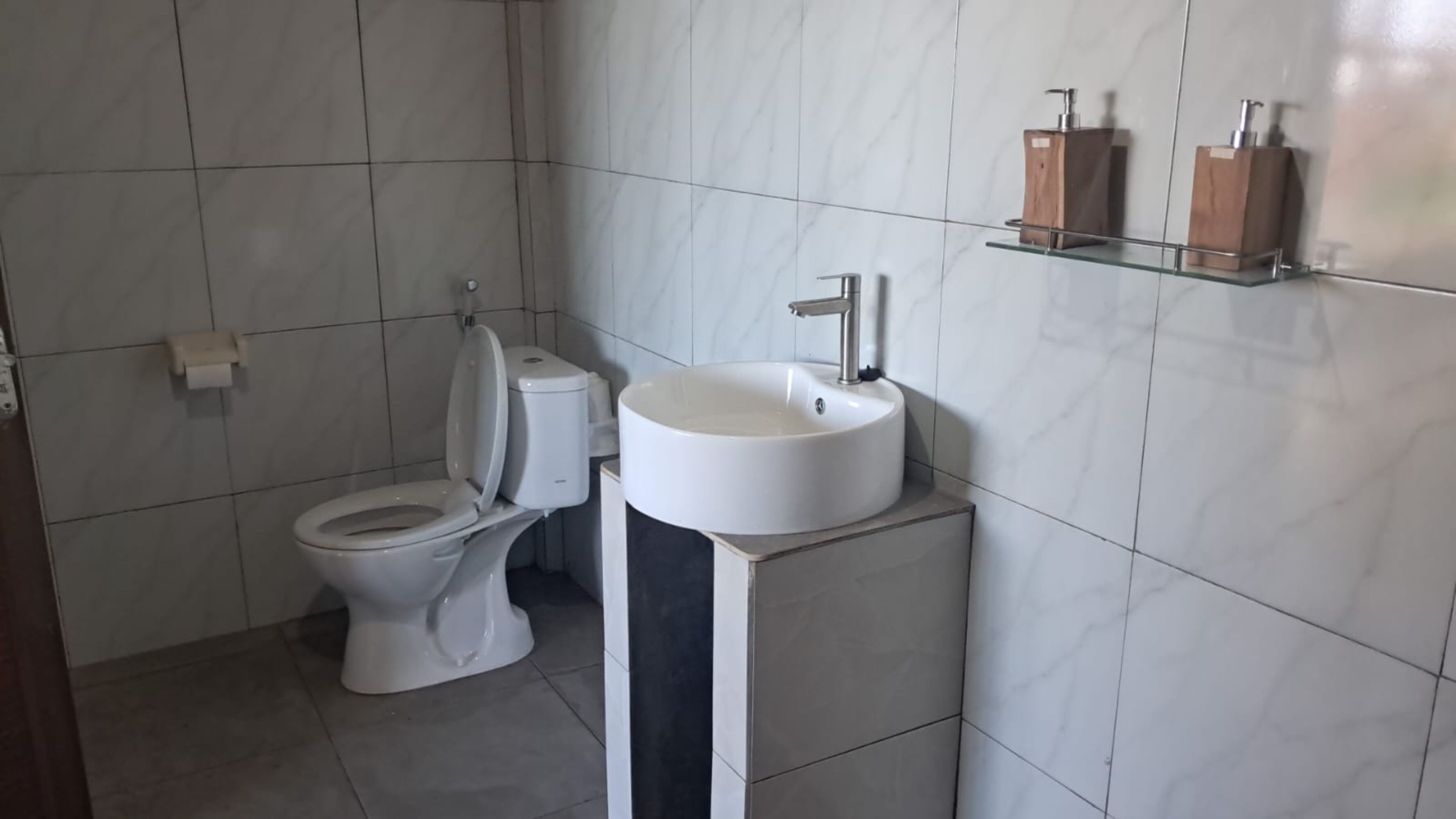 A bathroom with a toilet, a sink, and a shelf with toiletries.