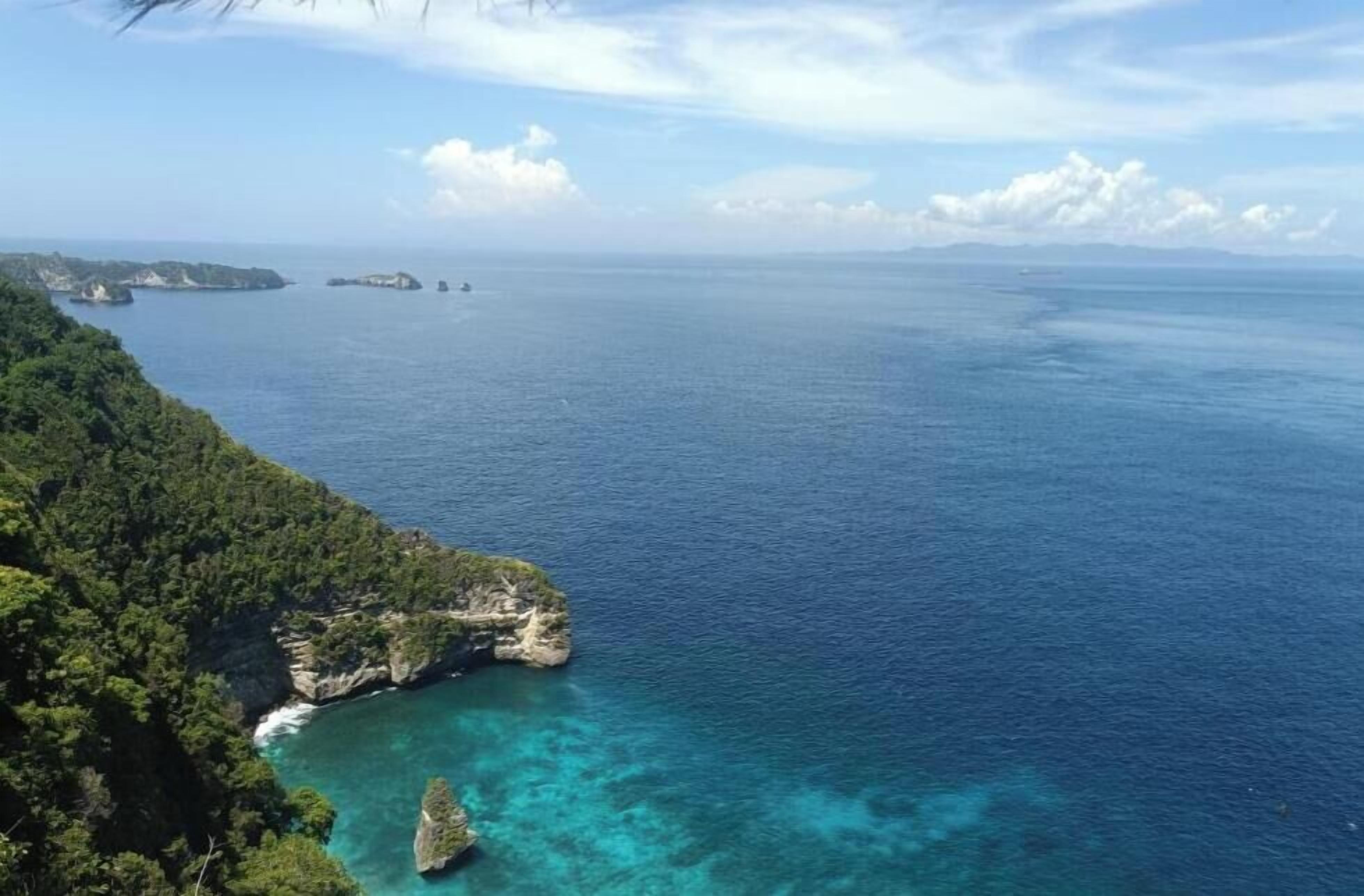 A coastal landscape with clear blue waters, rocky outcrops, and dense greenery.