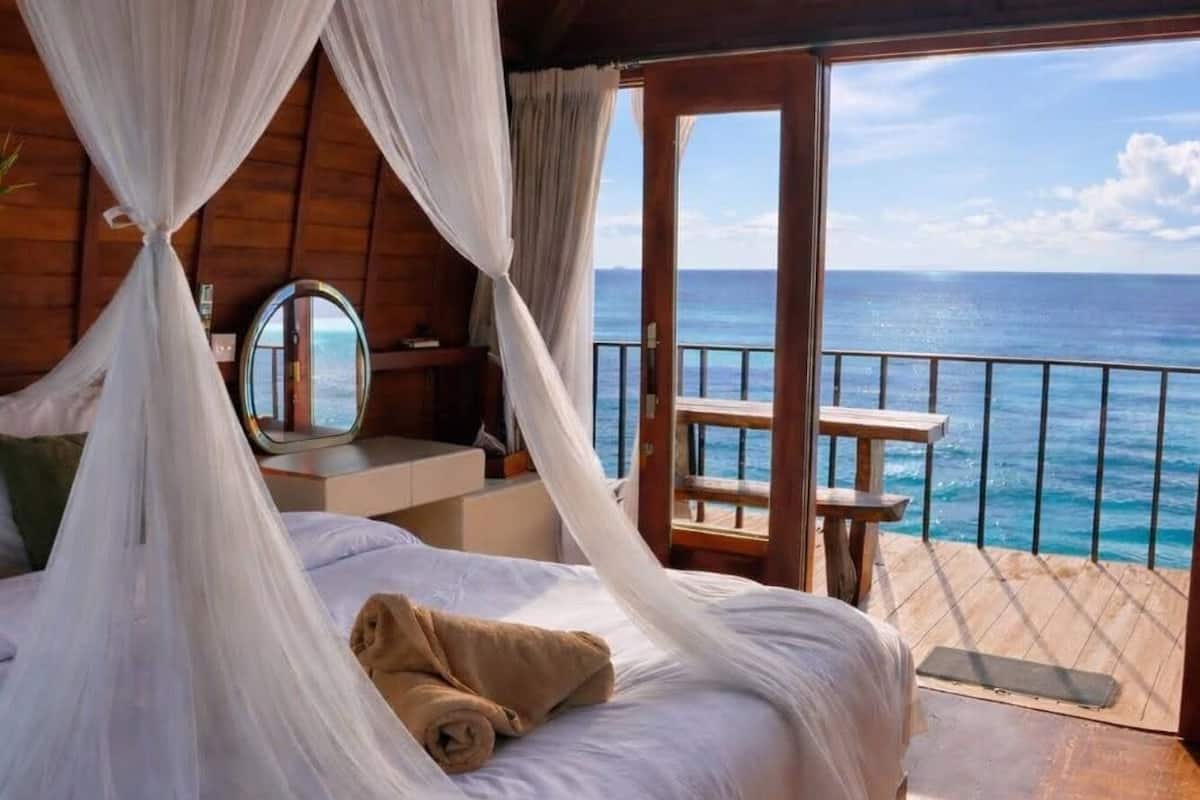 Un dormitorio con cama, mesita de noche, espejo y vista al océano.