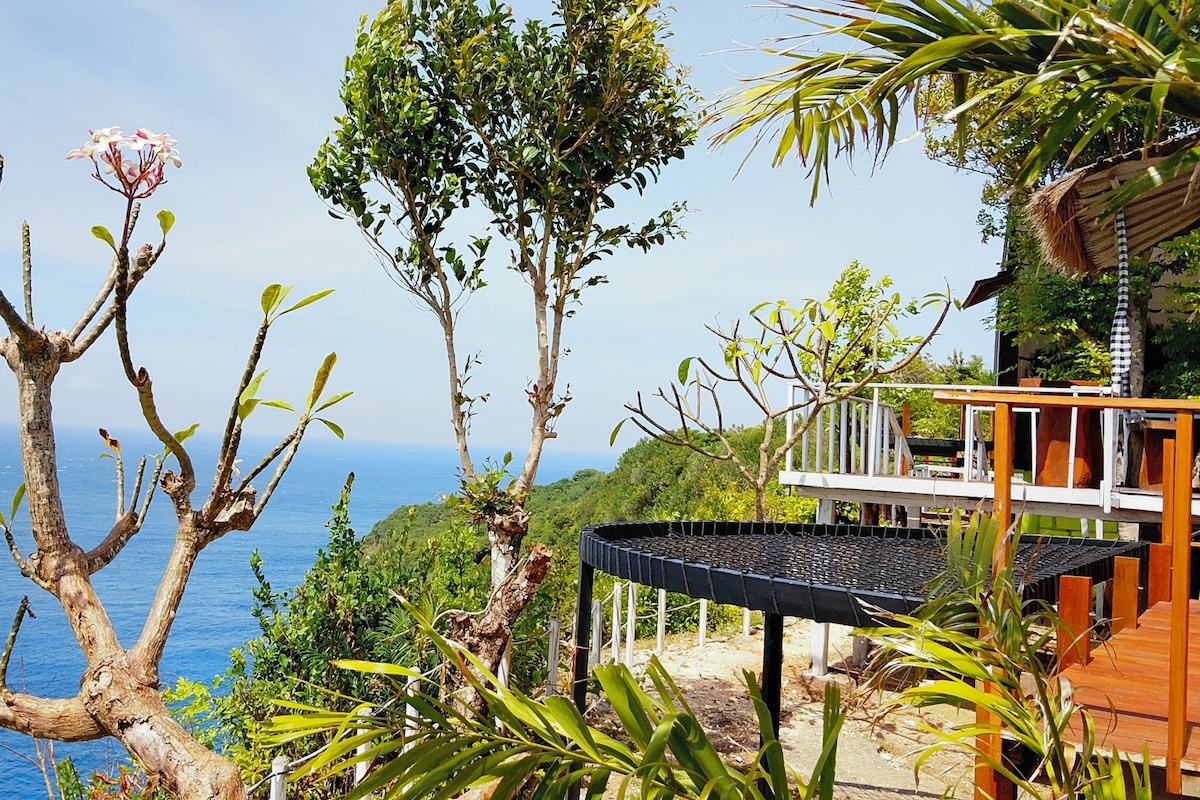 A coastal property with a view of the sea, a wooden deck, and a thatched roof structure.