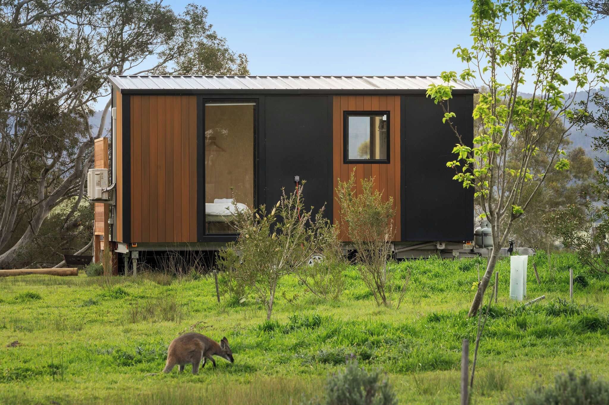 Une cabane moderne de plain-pied, dotée d’une grande porte coulissante, située dans un champ verdoyant, agrémenté d’arbres et offrant une vue sur un ciel dégagé.