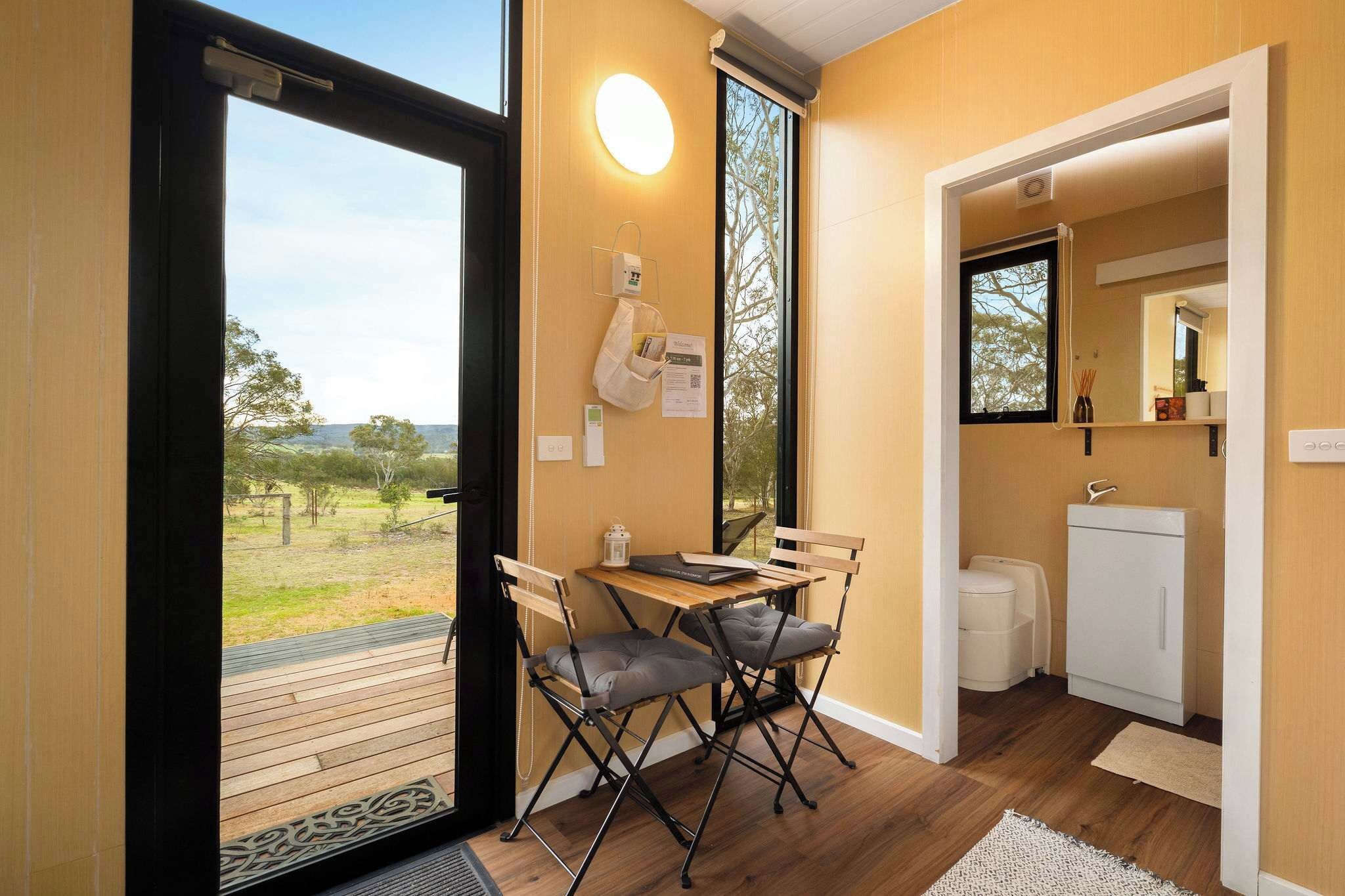 A room with a wooden table and chairs, a small kitchen area, and a door leading to an outdoor area.