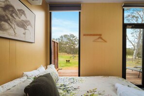 A bedroom with a bed, a painting, and a view of an outdoor area with a bench and trees.