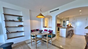 A modern kitchen with a dining area, built-in shelves, and a central island with stools. - Sea View Golf Retreat. Los Arqueros Benahavís (Benahavís)