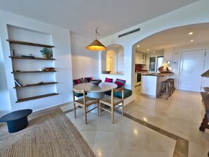 A modern kitchen with a dining area, built-in shelves, and a central island with stools. - Sea View Golf Retreat. Los Arqueros Benahavís (Benahavís)