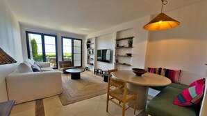 A modern living room with a sofa, a dining table, and a TV mounted on the wall. - Sea View Golf Retreat. Los Arqueros Benahavís (Benahavís)