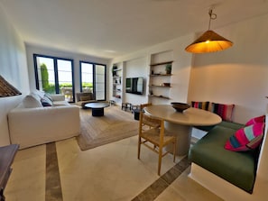 A modern living room with a sofa, a dining table, and a TV mounted on the wall. - Sea View Golf Retreat. Los Arqueros Benahavís (Benahavís)