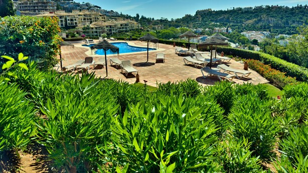 A pool area with lounge chairs and umbrellas, surrounded by greenery and overlooking a hillside. - Sea View Golf Retreat. Los Arqueros Benahavís (Benahavís)
