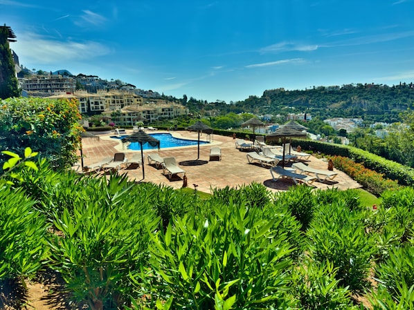 A pool area with lounge chairs and umbrellas, surrounded by greenery and overlooking a hillside. - Sea View Golf Retreat. Los Arqueros Benahavís (Benahavís)